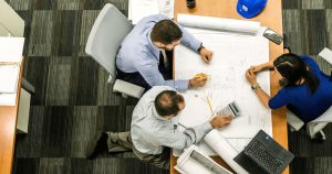 An overhead view of two men and a woman reviewing blueprints at a desk