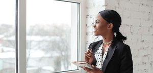 A young woman looking out a window while holding a tablet